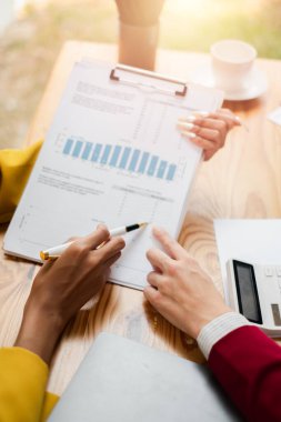 İyi ışıklandırılmış bir ofis ortamında yapılan bir iş toplantısında mali tablolar ve grafikleri tartışan iş arkadaşlarının yakın çekimleri.