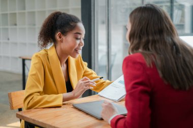Modern ofis ortamında finansal raporları analiz eden iki profesyonel kadın bir iş toplantısındalar..