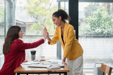 İki profesyonel kadın masa başında beşlik çakıyor, parlak ve modern ofis ortamında başarıyı kutluyorlar..
