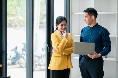 Modern ofis ortamında iki iş adamı, arka planda büyük pencereleri olan bir dizüstü bilgisayar kullanırken bir tartışmaya giriyorlar..