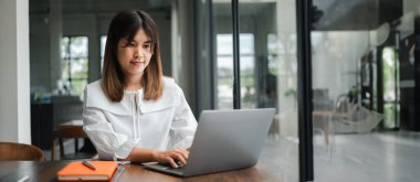 Modern bir ofis ortamında cam duvarlar ve modern mobilyalarla uğraşan genç profesyonel bir kadın..