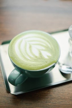 Karmaşık latte sanatıyla yakın plan bir matcha latte, ahşap bir masada yeşil bir fincanda servis ediliyor, kahve ve çay meraklıları için mükemmel..