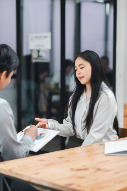 Modern ofis ortamında profesyonel meslektaşlar, bir iş toplantısında, bir pano üzerinde proje verilerini tartışıyor ve analiz ediyorlar..