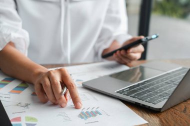 Modern bir ofisteki bilgisayar ve akıllı telefonla finansal tabloları ve grafikleri analiz eden bir iş adamının yakın plan fotoğrafı..