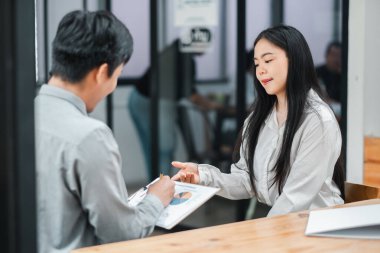 İki profesyonel, modern bir ofis ortamında doküman ve çizelgeleri gözden geçiriyorlar..