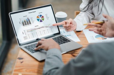 İki iş adamı, modern ofis ortamında takım çalışması ve analizi vurgulayarak bir dizüstü bilgisayarda finansal verileri tartışıyor..