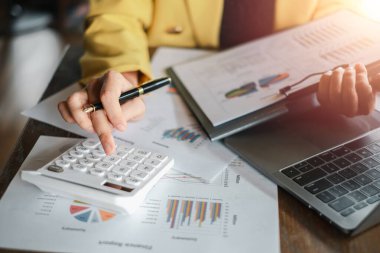 Bir iş adamı hesap makinesi kullanıyor ve bilgisayarlı bir masanın üzerindeki finansal çizelge ve grafikleri inceliyor..