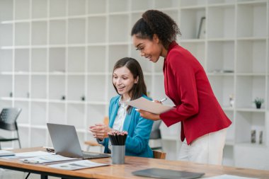 Çağdaş ofis ortamında birlikte çalışan iki profesyonel kadın, projeleri tartışıyor ve dizüstü bilgisayar kullanıyorlar..