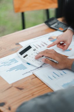 Tahta masadaki bir iş toplantısında hesap makinesi kullanarak ve mali raporları analiz ederek ellerinizi yakın plan yapın..