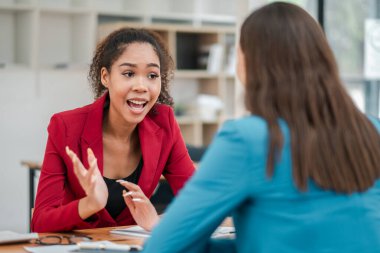 Çağdaş bir ofis ortamında masa başında sohbet eden iki profesyonel kadın..