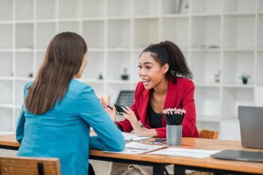 Modern ofis ortamında iş stratejilerini tartışan iki profesyonel kadın işbirliği ve takım çalışması sergiliyor..