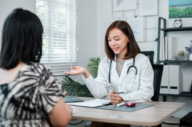 Beyaz önlüklü kadın doktor, modern bir muayenehanede bir hastaya danışarak, sağlık sorunları ve tedavi seçeneklerini tartışıyor..
