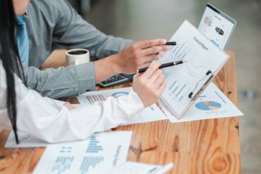 Modern bir ofis ortamında tablet ve kağıt belgeler kullanarak mali raporları ve veri analizini tartışan iki iş adamı.