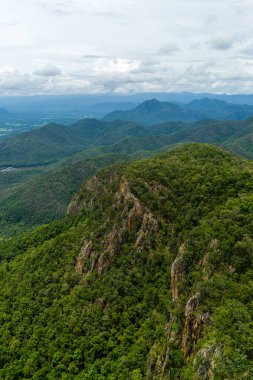 Arka planda bulutlu bir gökyüzü olan yoğun yeşil dağlar ve vadilerin sersemletici hava manzarası doğal güzellik ve sükuneti sergiliyor..