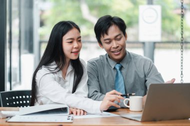 Modern bir ofiste çalışan iki genç profesyonel fikirleri tartışıyor ve bir dizüstü bilgisayar kullanıyorlar..