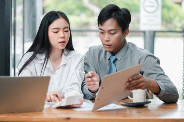 Modern ofis ortamında bir iş projesinde birlikte çalışan iki genç profesyonel, belgeleri tartışıyor ve bir dizüstü bilgisayar kullanıyor..