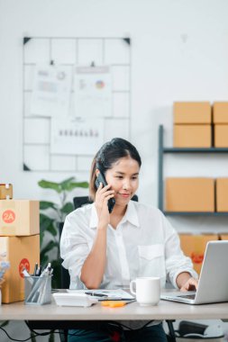 Modern bir ofiste birden fazla iş yapan genç bir girişimci. Laptopuyla çalışıyor ve telefonda konuşuyor. Etrafı kargo kutularıyla çevrili..