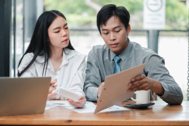 Modern ofis ortamında doküman ve çizelgeleri tartışan iki genç profesyonel, takım çalışması ve işbirliğine odaklanıyorlar..