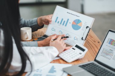 Çizelgeler ve grafikler üzerine pazar araştırma verilerini inceleyen iş adamları, modern bir ofis ortamında işbirliği yapıyorlar..