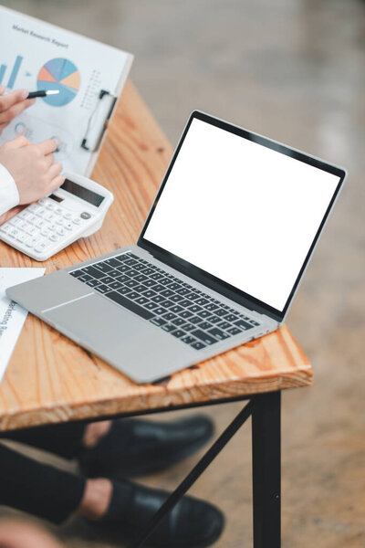 A business meeting setup featuring a laptop with a blank screen, a calculator, and graphs on a wooden table in a modern office environment.