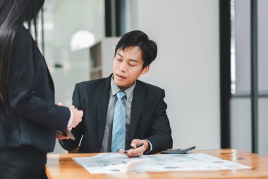 Takım elbiseli profesyonel Asyalı işadamı modern ofis ortamındaki bir meslektaşıyla belgeleri tartışıyor..