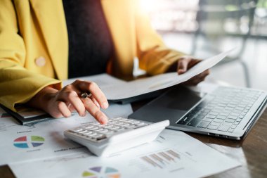 Finansal tabloları ve verileri hesap makinesi ve dizüstü bilgisayarla inceleyen profesyonel kadın, işletme ve finans kavramlarını ön plana çıkarıyor.