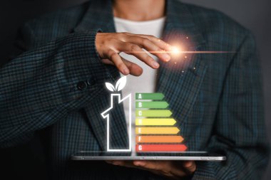 Takım elbiseli bir kişi enerji verimliliğini dijital enerji reytingleri göstererek sürdürülebilir ve çevre dostu uygulamaları vurguluyor..