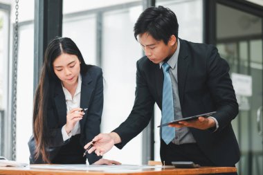 Modern ofis ortamında bir proje üzerinde çalışan resmi giyinmiş iki iş adamı..