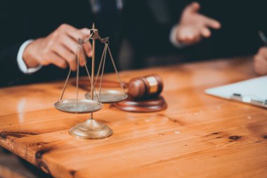 Avukatın elleri adalet terazisinin yanında ve ahşap bir masanın üzerindeki tokmak, hukuki tavsiye ve adaleti simgeliyor..