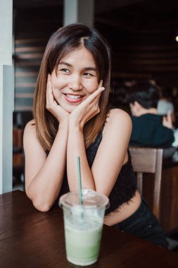 Neşeli bir gülüşü olan genç bir kadın sıcacık bir kafe ortamında ferahlatıcı bir içkinin tadını çıkarıyor, sıcak ve davetkar bir atmosfer yaratıyor..