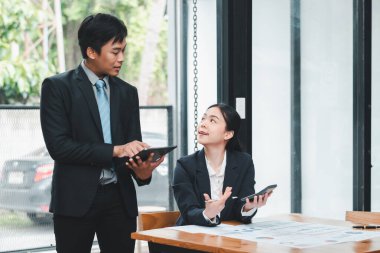 Modern ofis ortamında dijital cihazlar kullanarak resmi giyinmiş iki iş adamı iş hakkında konuşuyor..
