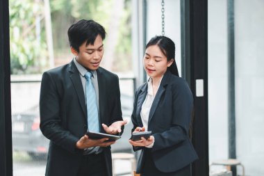 Modern ofis ortamında dijital tabletler kullanarak resmi giyinmiş iki iş adamı işi tartışıyor..