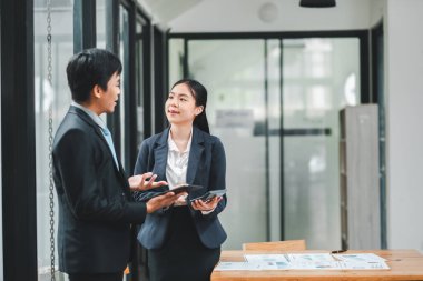 Resmi giyinmiş iki iş adamı modern bir ofiste belgeler ve tabletlerle tartışıyorlar..