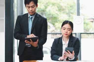 Modern ofis ortamında dijital cihazlar kullanarak resmi giyinmiş iki iş adamı birlikte çalışıyor..