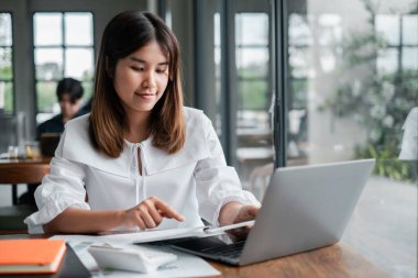 Modern ofis ortamında dizüstü bilgisayarda çalışan genç bir kadın, doğal ışık ve çağdaş dekor ile çevrili..