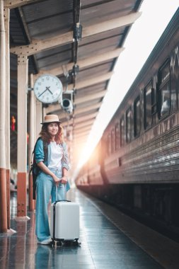 Bavullu genç bir kadın gün doğumunda tren istasyonunda hazır bekliyor. Günlük giysiler ve şapkalar giyer, yolculuğunu dört gözle bekler..