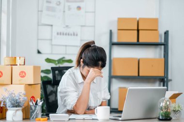 Ev ofisinde çalışırken strese giren bir kadın. Çevresi dizüstü bilgisayarla çevrili ve çevrimiçi işi için paket kutularıyla çevrili..