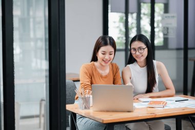 Çağdaş bir ofiste birlikte çalışan iki kadın dizüstü bilgisayar kullanıyor ve belgeleri inceliyor..