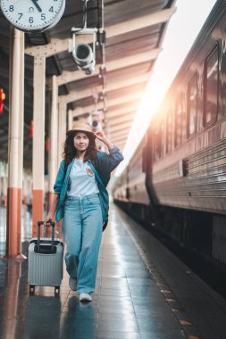 * * Şık bir genç kadın, bavuluyla bir tren istasyonunda, sıcak gündoğumu ışığında güvenle yürür.