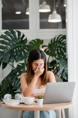 Modern bir ofis ortamında, bitkilerle çevrili bir şekilde, masa başında hapşıran bir kadın..