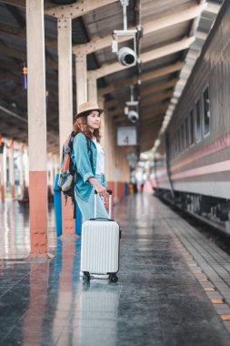 Bavullu genç bir gezgin, heyecan verici bir yolculuğa hazır bir tren istasyonunda duruyor. Günlük kıyafet ve sırt çantası macerayı akla getiriyor..