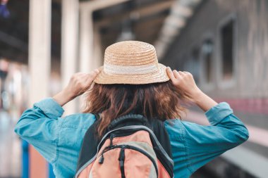Sırt çantası ve hasır şapkalı bir kişi tren istasyonunda durur, seyahat ve keşif için hazırdır..