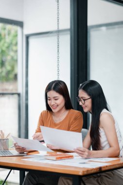 Masada birlikte çalışan iki genç kadın, parlak ve modern bir ofis ortamında belgeleri gözden geçiriyorlar..