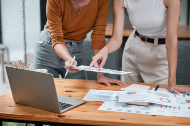 Çağdaş bir ofis ortamında proje detaylarını çizelge ve dizüstü bilgisayarla tartışan iki profesyonel.