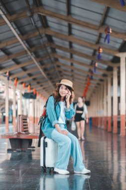 Kot pantolon ve şapka giymiş neşeli bir gezgin tren istasyonunda oturmuş, maceraya hazır..