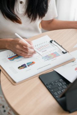 Finansal tablolar ve grafikleri bir tablet ve kağıtta inceleyen, iş analizlerini ve veri yorumlarını vurgulayan bir kadının yakın çekimi.