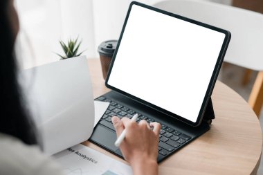 Belgeler ve küçük bir bitkiyle çevrili boş ekranlı dijital tablet üzerinde çalışan kişi..