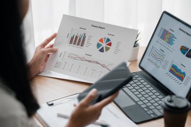 Modern ofis ortamında veri analizini gösteren, dizüstü bilgisayarında ve kağıtta grafiklerle finansal raporları inceleyen bir profesyonel..