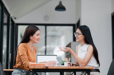 Çağdaş ofis ortamında iş stratejilerini tartışan iki kadın, takım çalışması ve işbirliği sergiliyor.