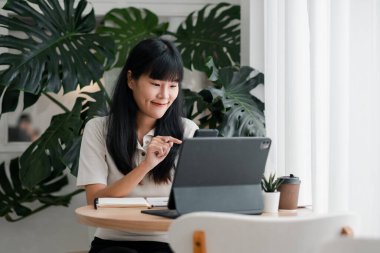 Genç bir kadın, yemyeşil bitkiler ve doğal ışıkla çevrili, parlak bir ofis ortamında tablet kullanıyor..